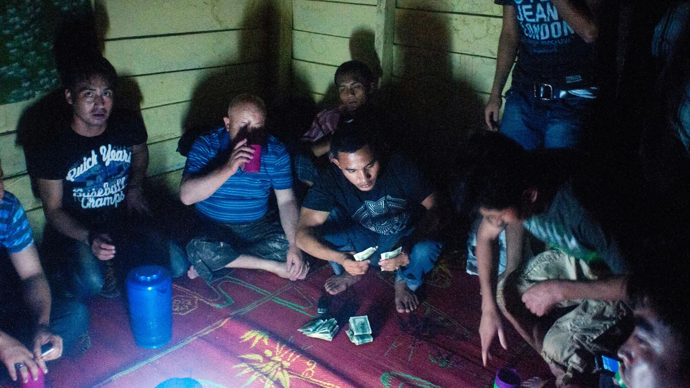 Men resting on a mat in a dark timber house in Sumatra, banknotes on the floor between them, 2012.
