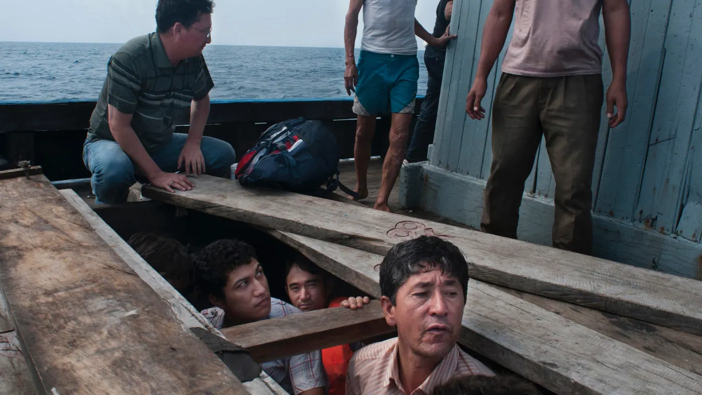 Men look up through an open hatch from below the deck of a wooden fishing boat at sea, others standing above, 2012.
