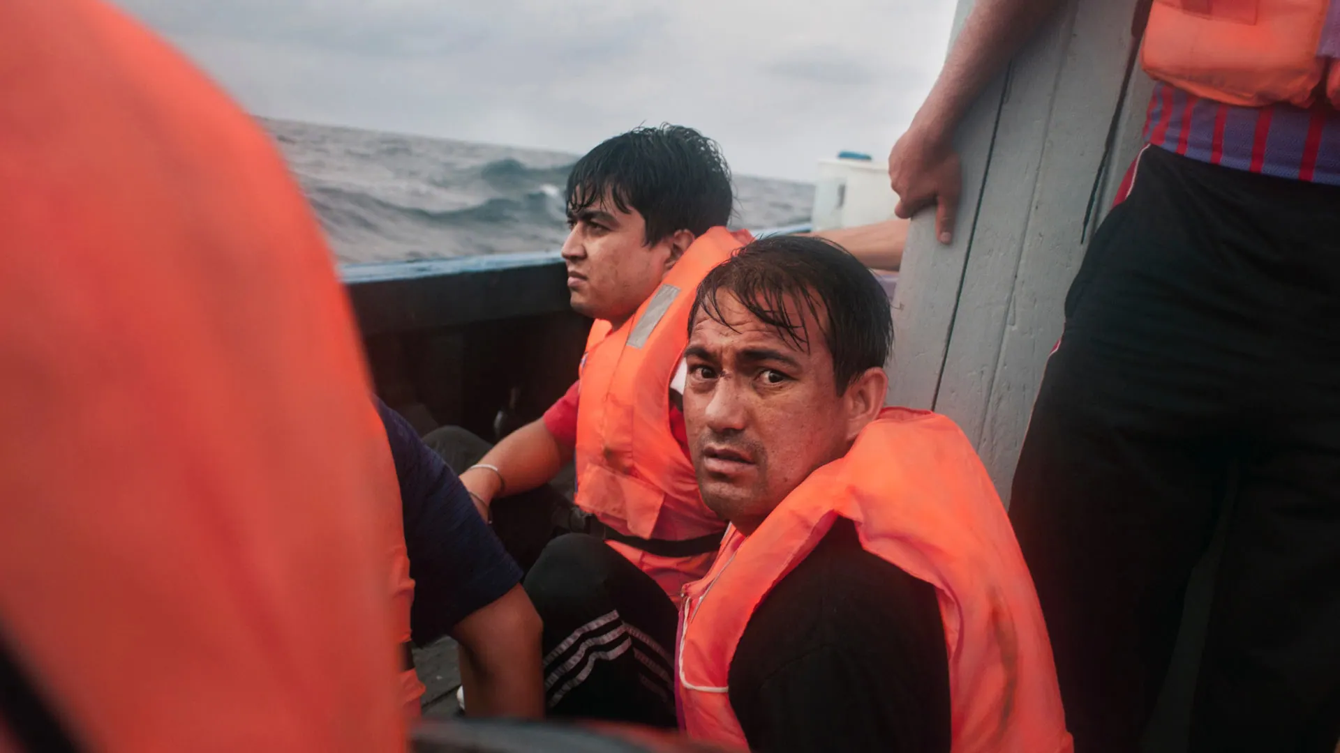 Two men in orange life jackets aboard the boat in rough grey seas, 2012.