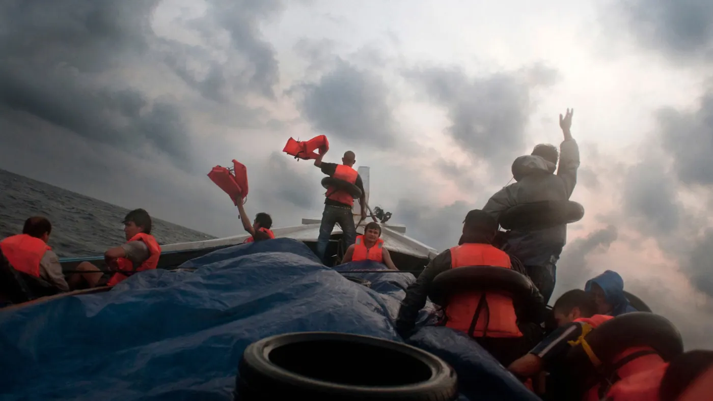 People on the boat waving red life jackets at a stormy sky to attract a passing ship, Indian Ocean, 2012.