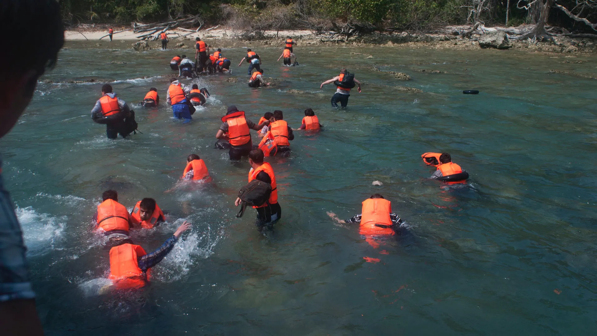 People in orange life jackets wading ashore through shallow water towards the jungle at Ujung Kulon, 2012.